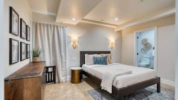 A bedroom with a bed, bedside tables, a small plant, a rug, and wall-mounted lights.