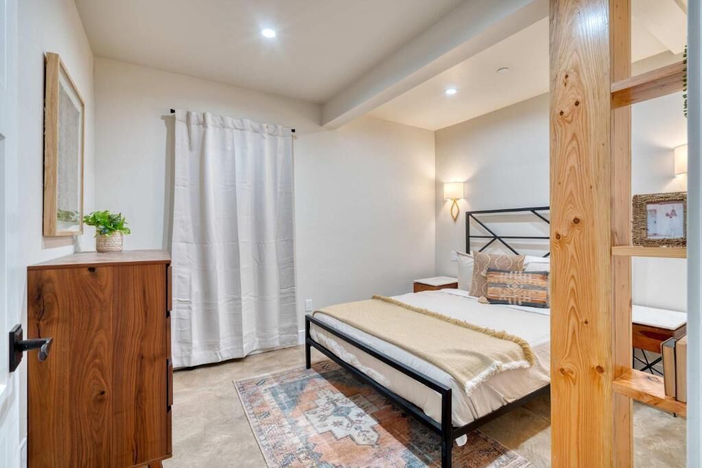 A bedroom with a bed, a wooden cabinet, a wall-mounted lamp, and a patterned rug.