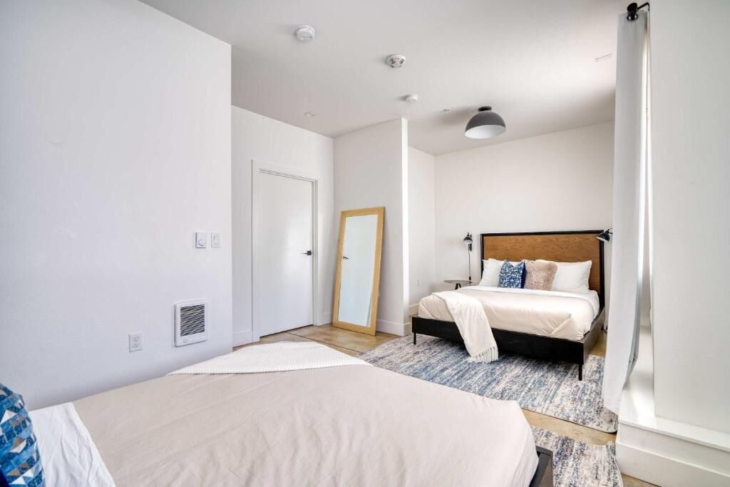 A bedroom with a bed, a bedside table, a mirror, and a window.