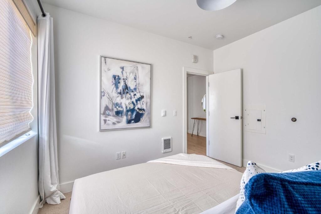 Un dormitorio moderno con una cama, una puerta que da a otra habitación y una ventana con persianas.