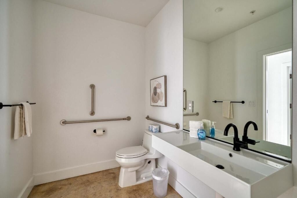 A bathroom with a white toilet, a sink with a mirror, and grab bars on the walls.