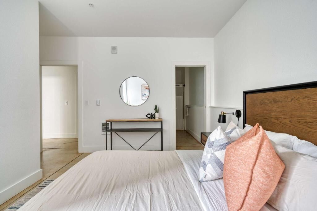 A bedroom with a bed, bedside table, mirror, and a view into the hallway.