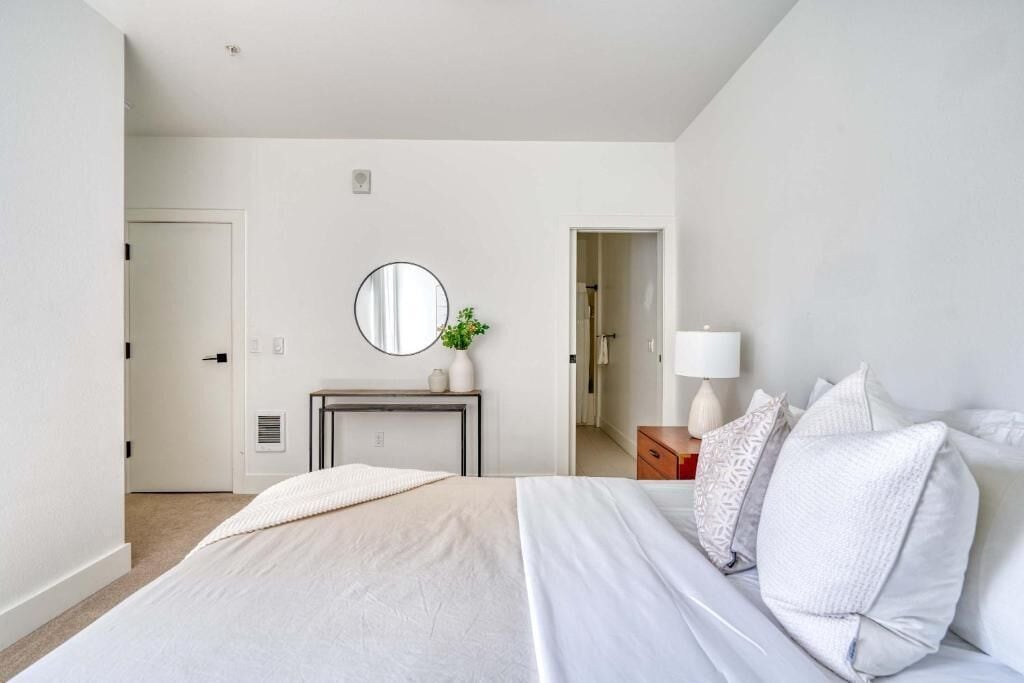 A bedroom with a bed, bedside table, lamp, and a mirror on the wall.
