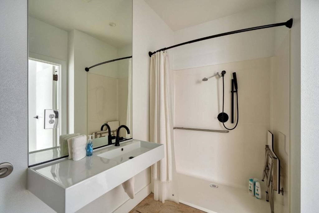 Een badkamer met een wit wastafelmeubel, een spiegel, een douche met een zwart gordijn en een handdoekhouder.