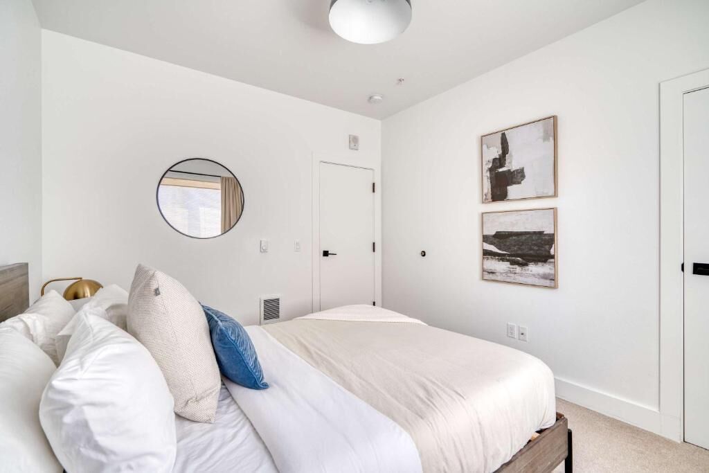 Une chambre à coucher avec un lit, des oreillers, un miroir rond, une porte et des œuvres d’art accrochées au mur.