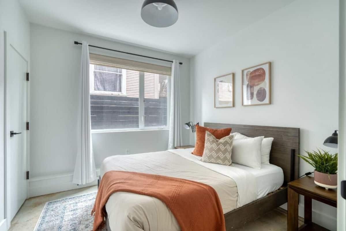 A bedroom with a bed, a window, a door, and a nightstand with a lamp.