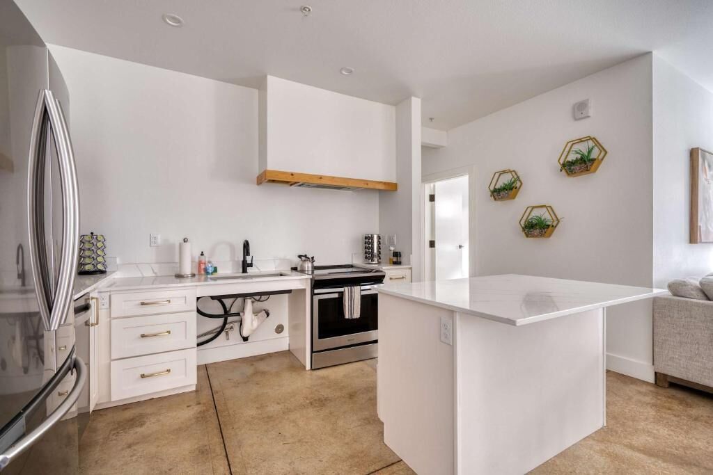 A modern kitchen with white cabinetry, a stainless steel refrigerator, a built-in oven, and a small island.