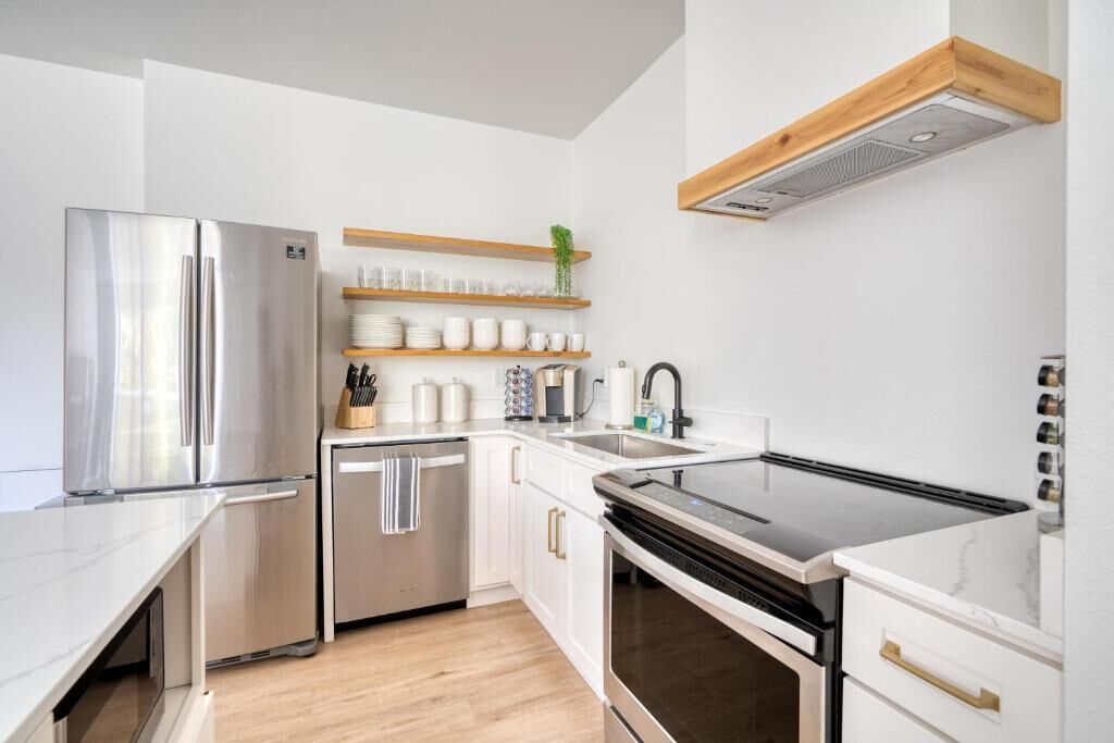 A modern kitchen with a stainless steel refrigerator, a dishwasher, a black induction cooktop, and white cabinetry.