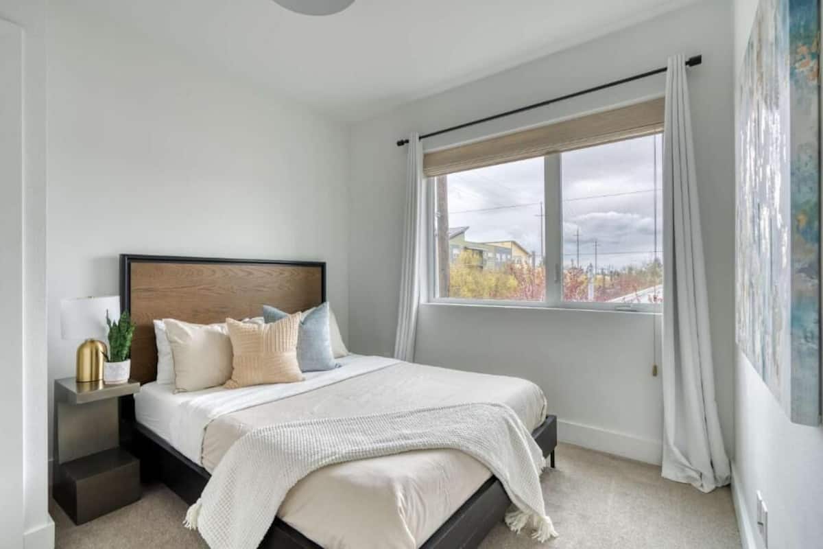 A bedroom with a bed, bedside table, and a window with curtains.