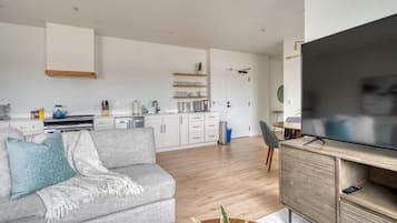 A modern living room with a sofa, a coffee table, a TV, and a kitchen in the background.