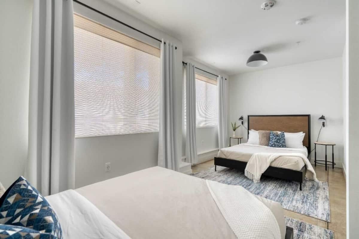 A modern bedroom with a large bed, a smaller bed, and a desk with a lamp.