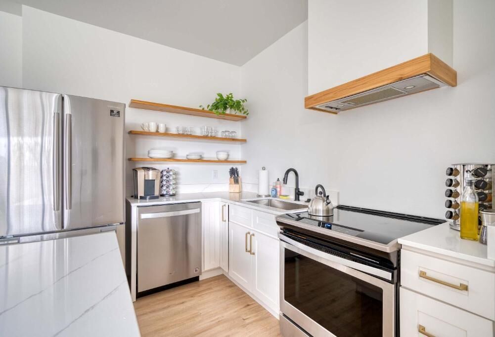 Una cocina moderna con electrodomésticos de acero inoxidable, repisas de madera y horno empotrado.