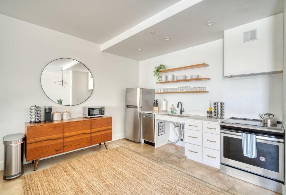 A modern kitchen with a wooden cabinet, stainless steel appliances, and a round mirror.