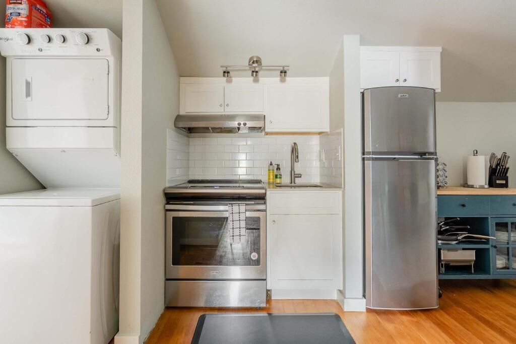 Una cocina compacta con armarios blancos, un horno de acero inoxidable, un microondas integrado y un refrigerador.