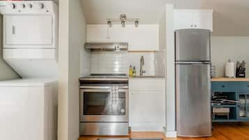 Una cocina compacta con armarios blancos, un horno de acero inoxidable, un microondas integrado y un refrigerador.