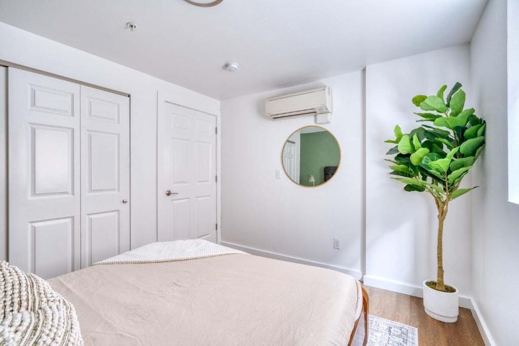 A bedroom with a bed, white walls, a round mirror, and a potted plant.