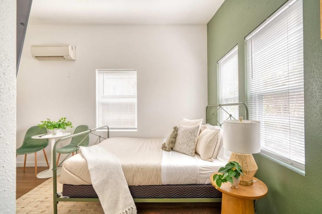 A bedroom with a bed, bedside table, lamp, and a window with blinds.