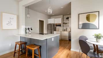 A modern kitchen with a central island, wooden stools, and a dining area with a table and chairs.