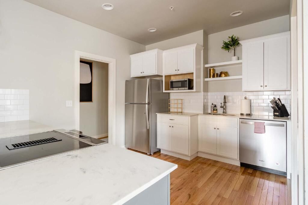 A modern kitchen with white cabinetry, stainless steel appliances, and a wooden floor.