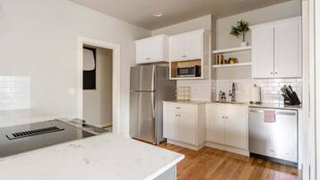 A modern kitchen with white cabinetry, stainless steel appliances, and a wooden floor.