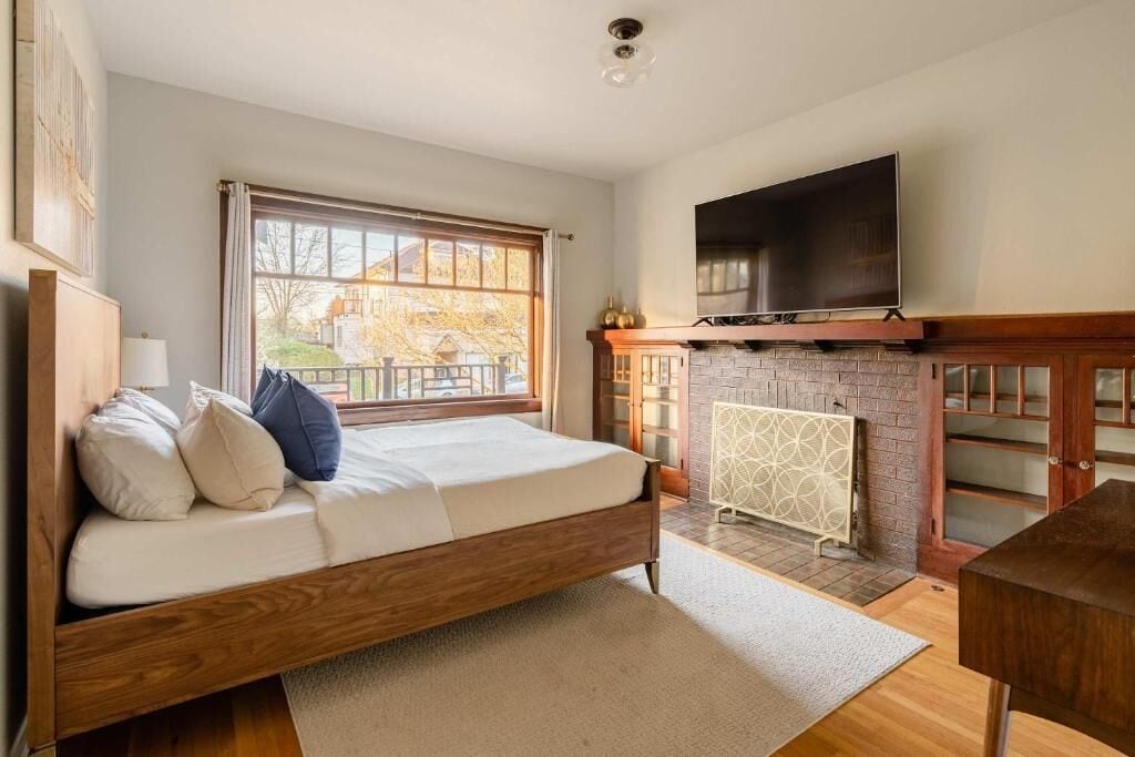 A bedroom with a bed, a television, a fireplace, and a window.