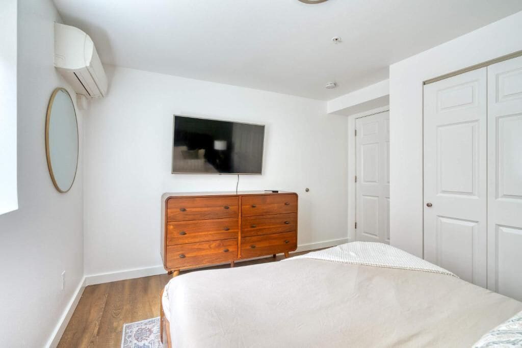 A bedroom with a wooden dresser, a bed, a television on the wall, and white doors.