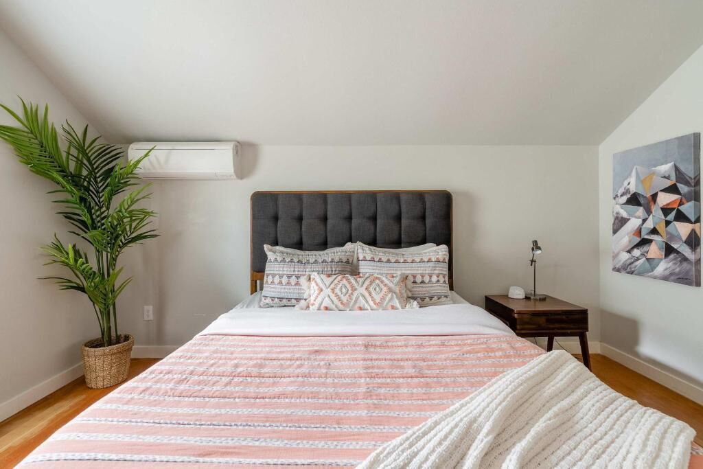Un dormitorio con una cama, una planta en maceta, una mesita de noche y un aire acondicionado de pared.
