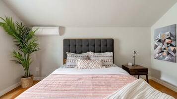 Un dormitorio con una cama, una planta en maceta, una mesita de noche y un aire acondicionado de pared.