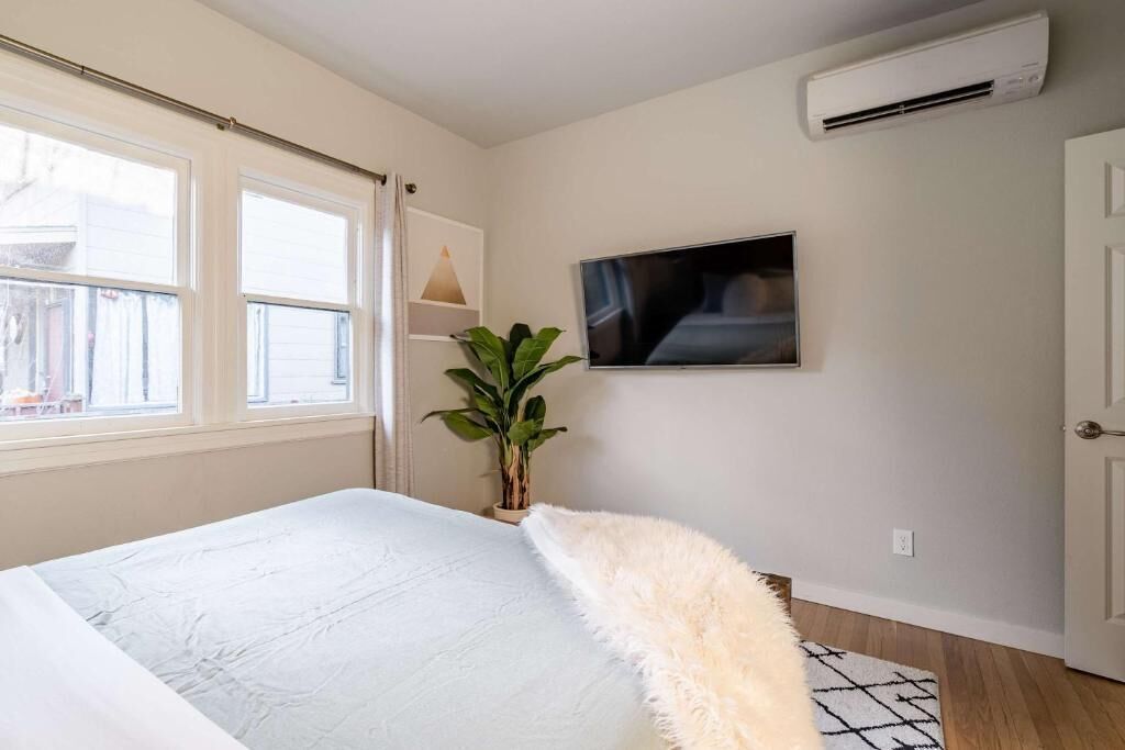 Ein Schlafzimmer mit einem Bett, einem Fernseher, einer Klimaanlage, einem Fenster und einer Pflanze.
