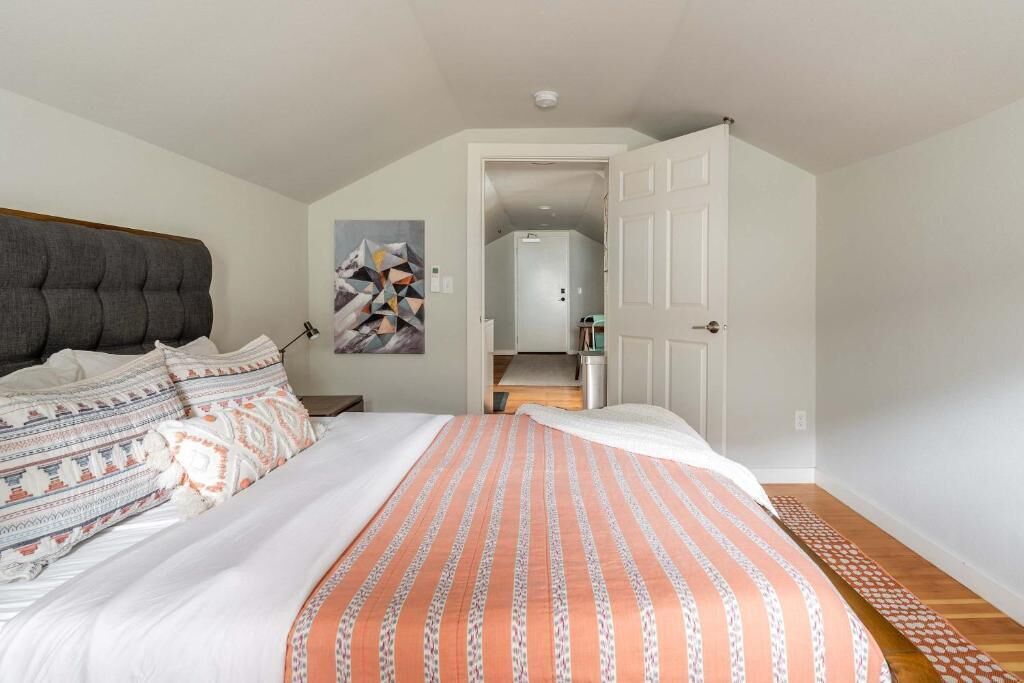 Une chambre à coucher avec un lit, une tête de lit, un tableau, une porte et un couloir.