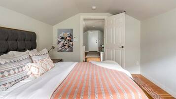 Une chambre à coucher avec un lit, une tête de lit, un tableau, une porte et un couloir.