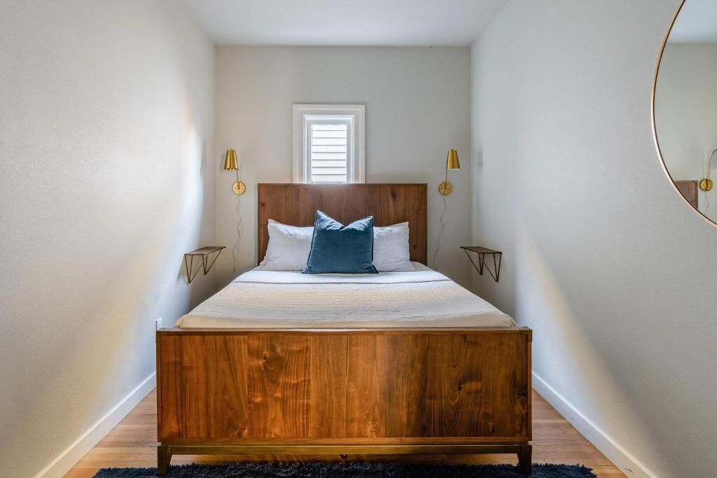 A bedroom with a wooden bed, two bedside tables, a window, and wall-mounted lamps.