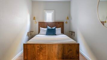 A bedroom with a wooden bed, two bedside tables, a window, and wall-mounted lamps.