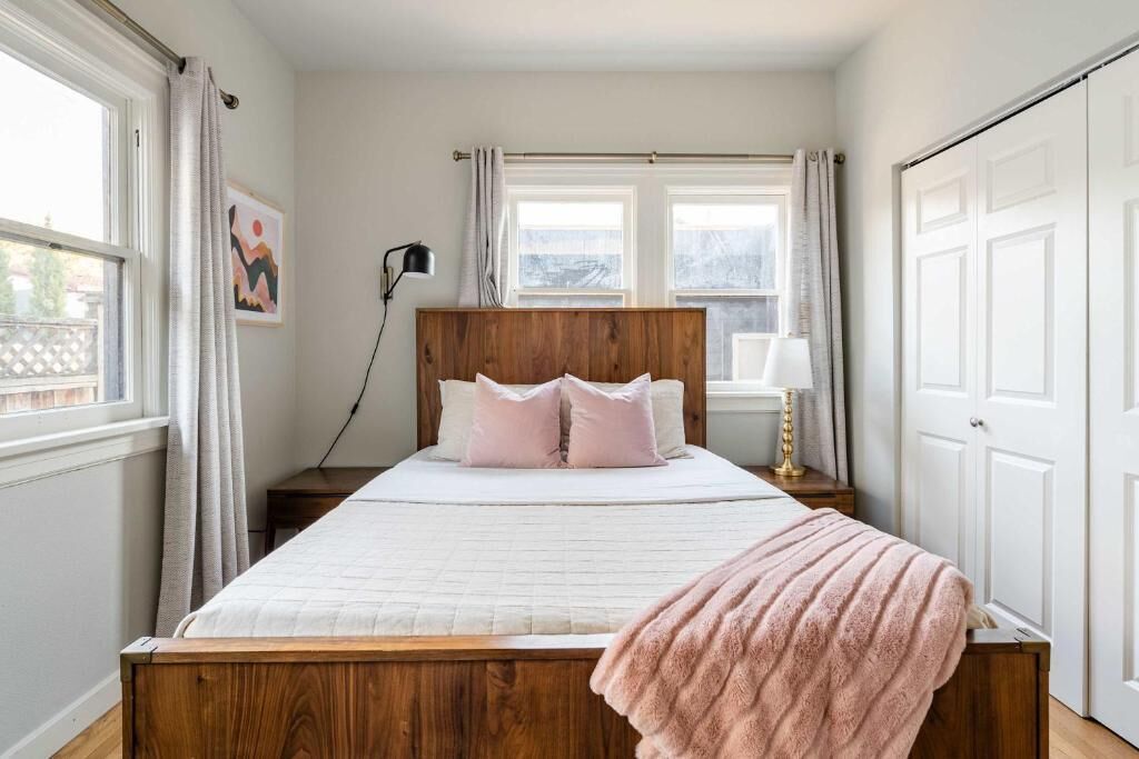 Une chambre à coucher avec un lit en bois, du linge de lit blanc, une lampe de chevet et une fenêtre avec des rideaux.