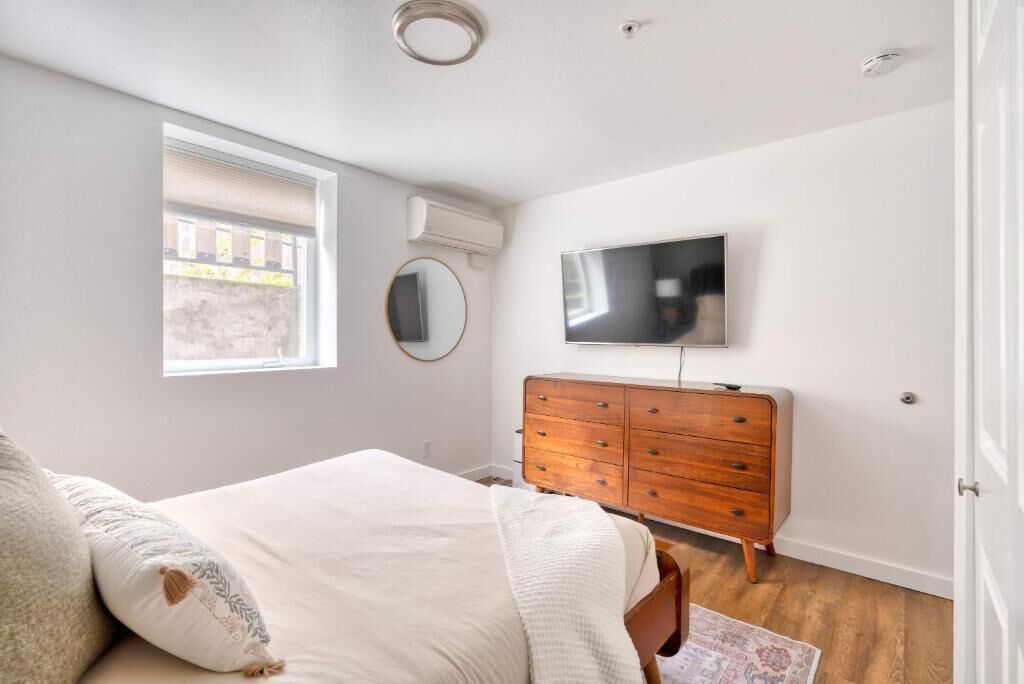 Une chambre à coucher comprenant un lit, une commode, un téléviseur, une fenêtre et un appareil de climatisation.