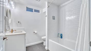 A bathroom with a white sink, mirror, toilet, and shower area.