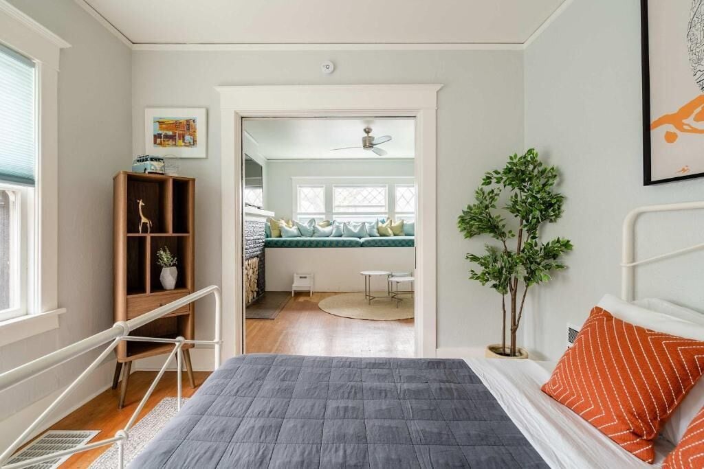 A bedroom with a bed, a wooden shelf, a small table, and a potted plant.