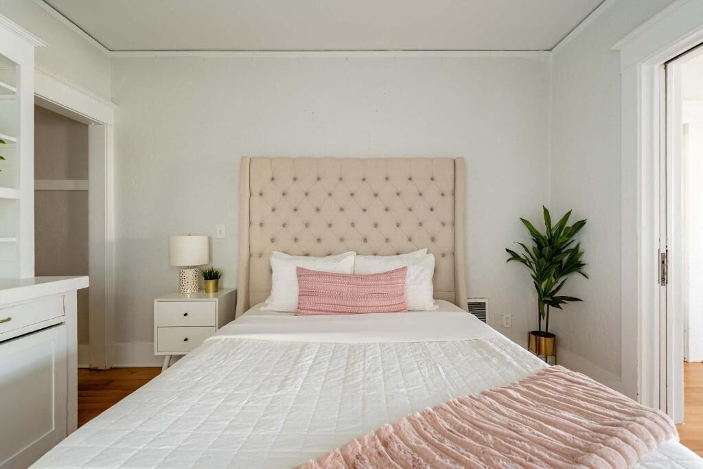 A bedroom with a bed, bedside table, lamp, and a potted plant.