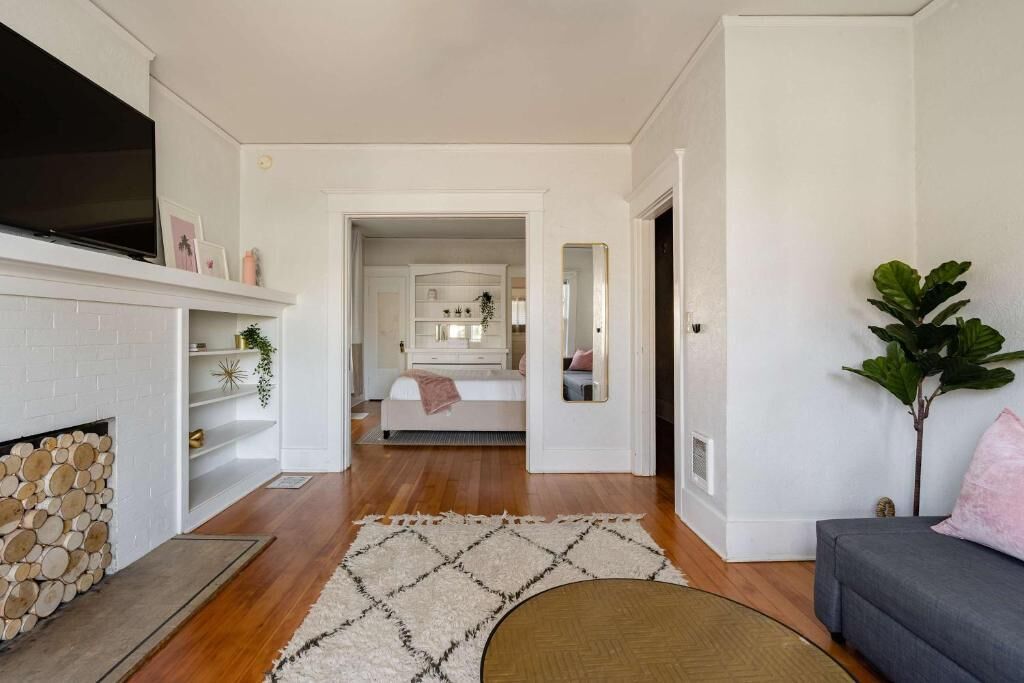 A living room with a fireplace, a sofa, a coffee table, and a hallway leading to a bedroom.