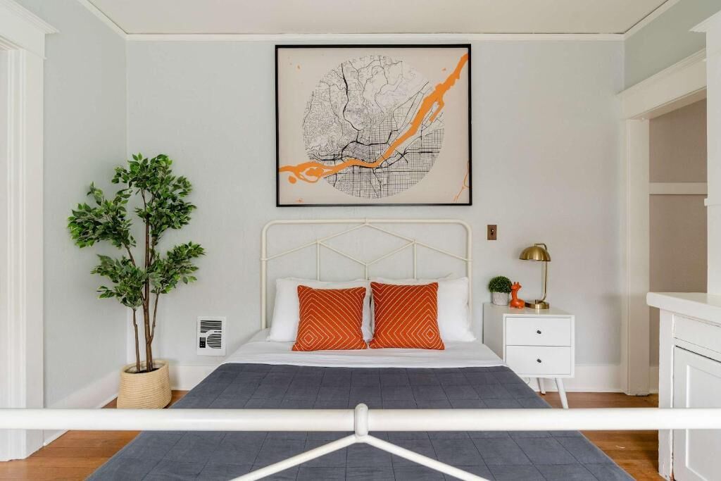 A bedroom with a bed, a nightstand, a lamp, a plant, and a framed map on the wall.
