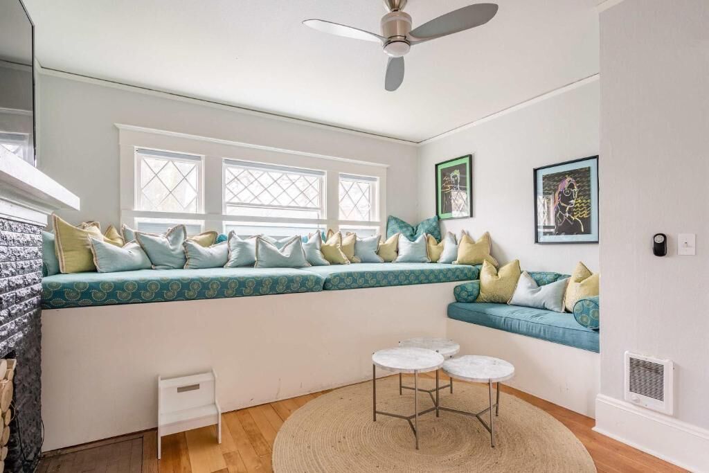 A room with a built-in bench, two small tables, a ceiling fan, and a window with a view.