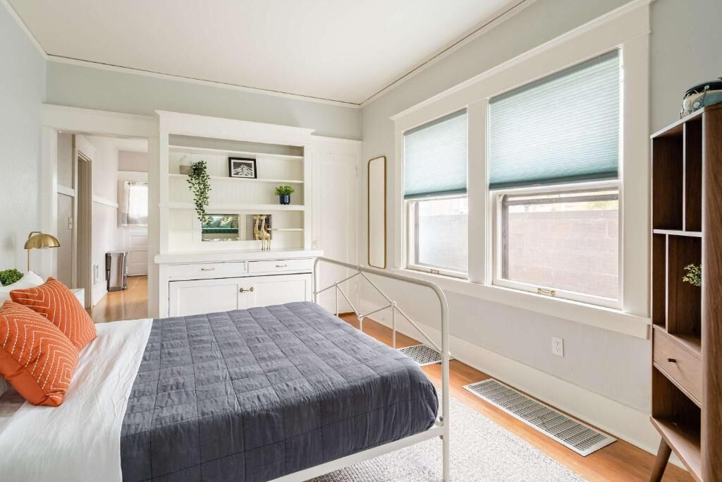 A bedroom with a bed, a dresser, a vanity, and a window with blinds.