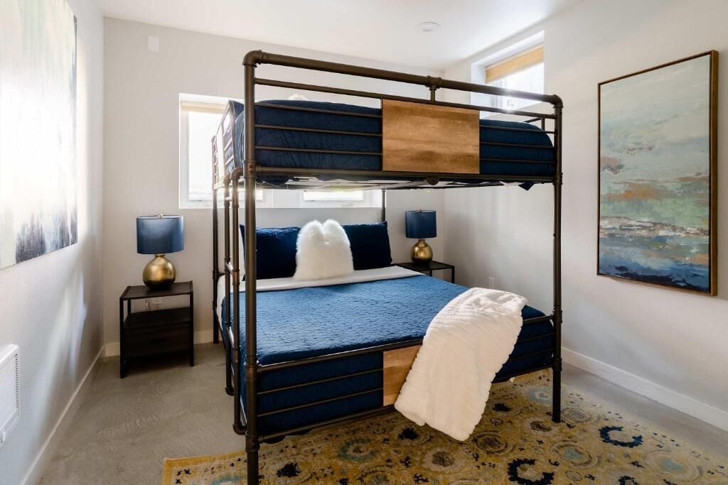 Un lit superposé avec un matelas bleu, un plaid blanc, deux lampes de chevet et un tapis à motifs.