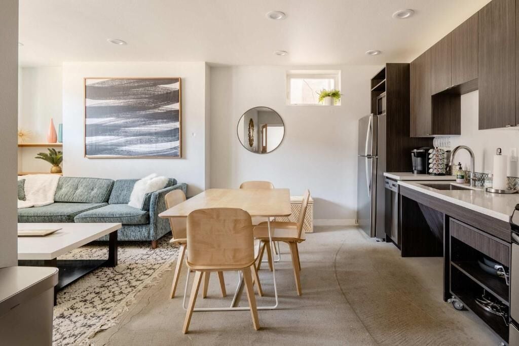 A modern kitchen with dark wood cabinets, a stainless steel refrigerator, and a dining area with a wooden table and chairs.