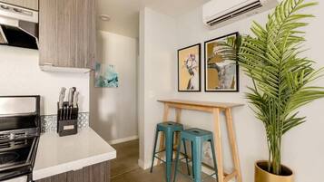Una cocina con estufa, encimera y juego de cuchillos. Hay dos taburetes y una planta en maceta.
