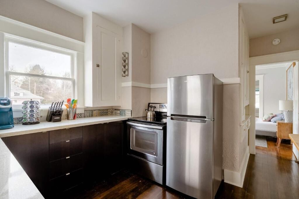 A modern kitchen with dark cabinetry, stainless steel appliances, and a window providing natural light.
