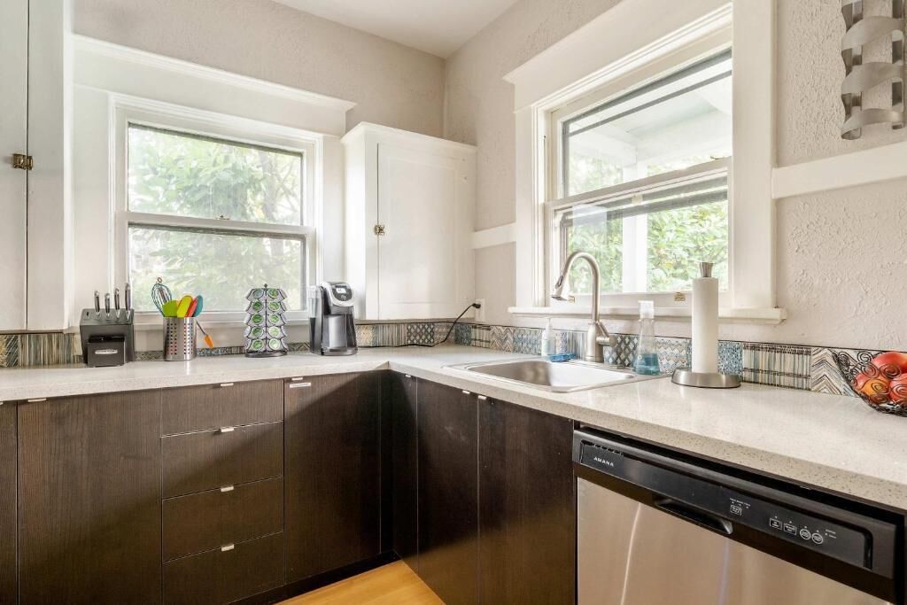 A kitchen with dark cabinets, a dishwasher, a sink, and a window.