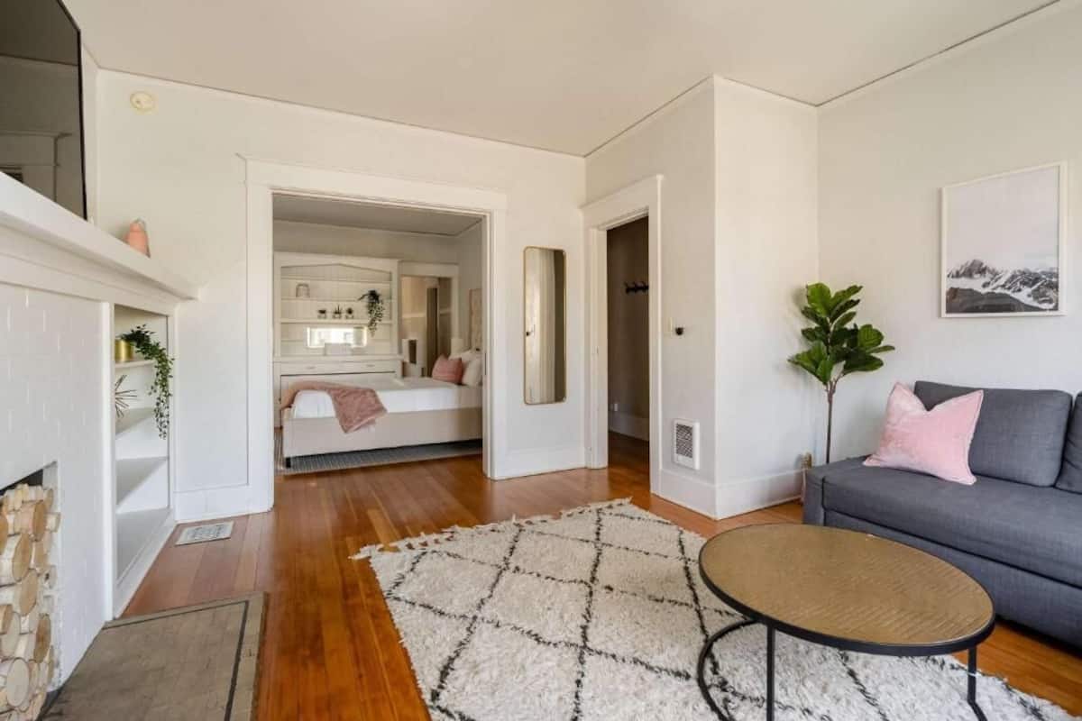 Una sala de estar con sofá, mesa de centro, chimenea y una escalera que lleva a un dormitorio.