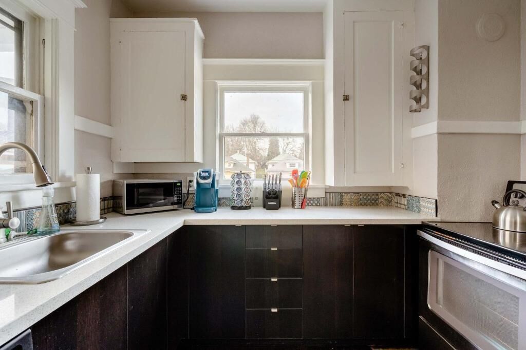 A kitchen with a window, a sink, a microwave, and cabinets.