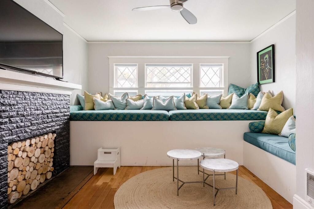 A cozy room with a built-in bench, a fireplace, a ceiling fan, and a small table with chairs.
